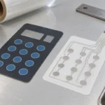Illustration of a membrane-switch graphic overlay and a separate silver-printed circuit film on an inspection bench